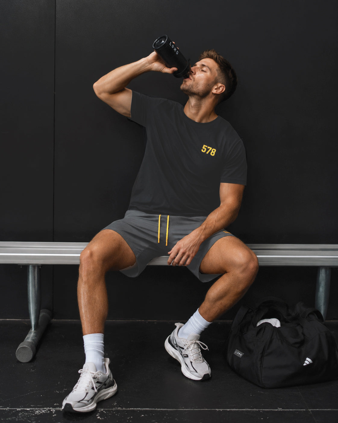 Male model wearing the Sauce & Brown Carbon 578 black performance sports t-shirt and Quarry dark grey marl jogger shorts during a break at the gym.