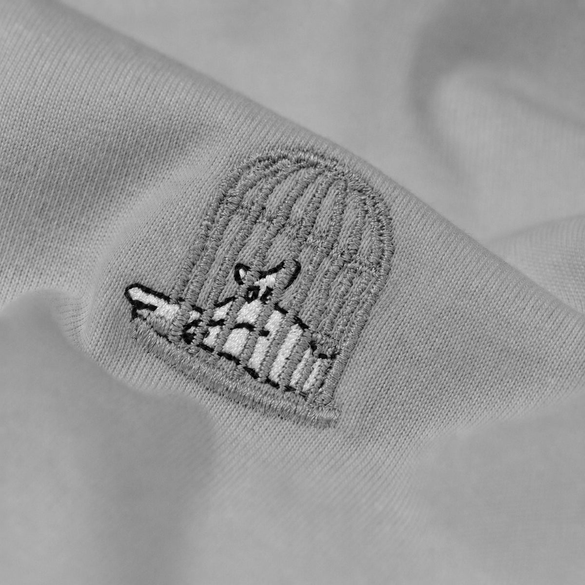 Close-up of the embroidered birdcage logo on the Sauce & Brown Haze oversized t-shirt