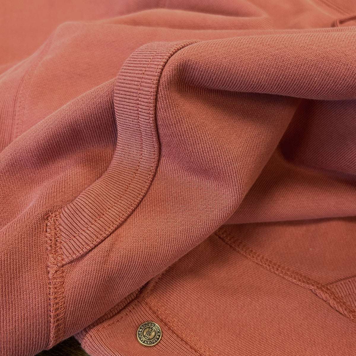 Close-up of the Sauce & Brown Kiln Hoody in Vintage Washed Terracotta, showing the heavyweight cotton fabric, ribbed detailing, reinforced stitching and signature numbered metal rivet.