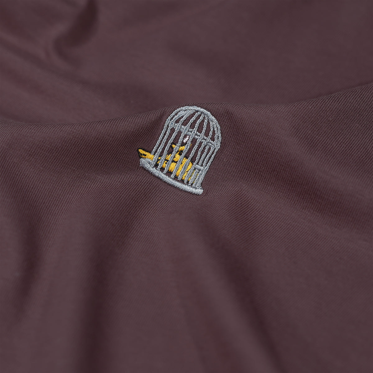 Embroidered design of a bird in a cage on a brown fabric background
