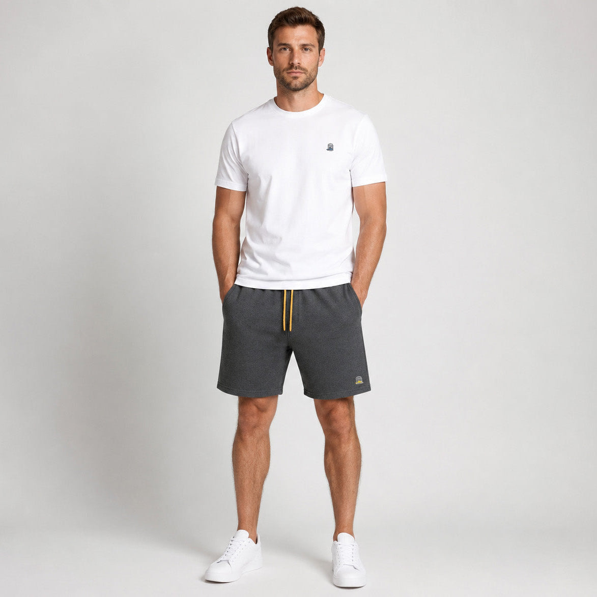 Front studio photograph of a male model wearing the Sauce & Brown Quarry dark grey marl jogger shorts with canary yellow drawcord and embroidered birdcage logo.