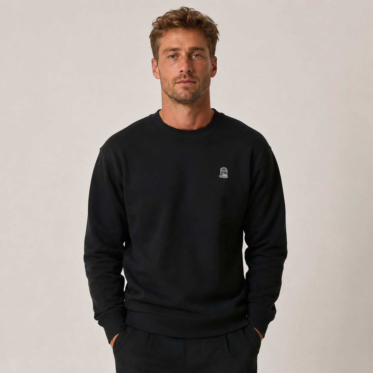 Men’s black organic cotton sweatshirt worn in studio lifestyle portrait with relaxed fit and subtle chest embroidery