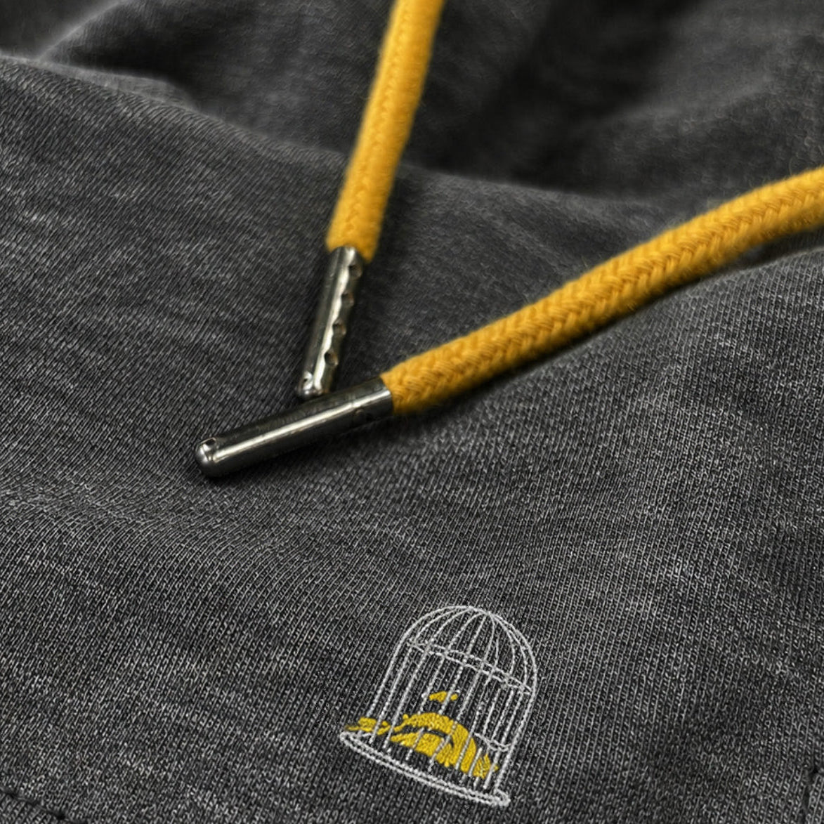 Close-up of the Sauce & Brown Quarry dark grey marl jogger shorts showing the canary yellow drawcord, marl fabric and embroidered birdcage logo.