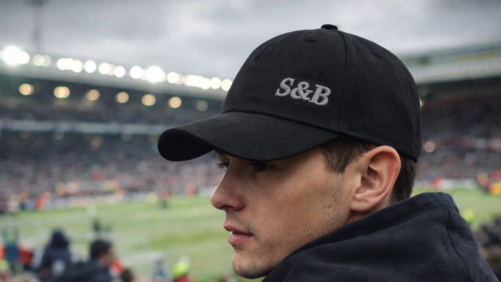 Model wearing Away Days Cap in black at football stadium by Sauce & Brown
