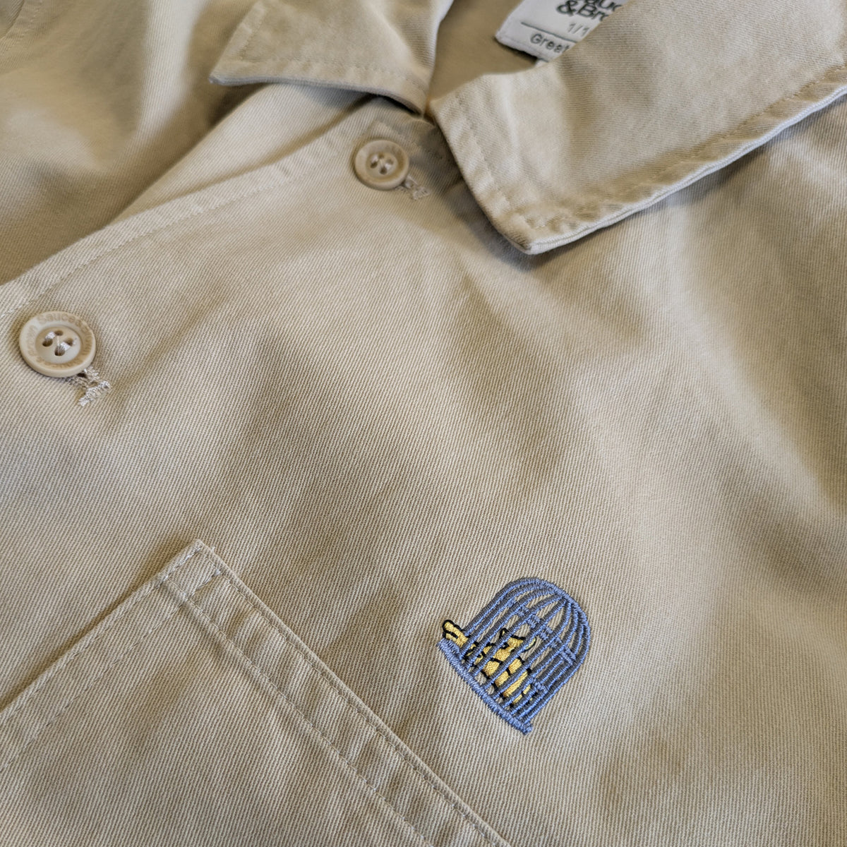 Close-up embroidered logo detail on Bourne Jacket in sand by Sauce & Brown