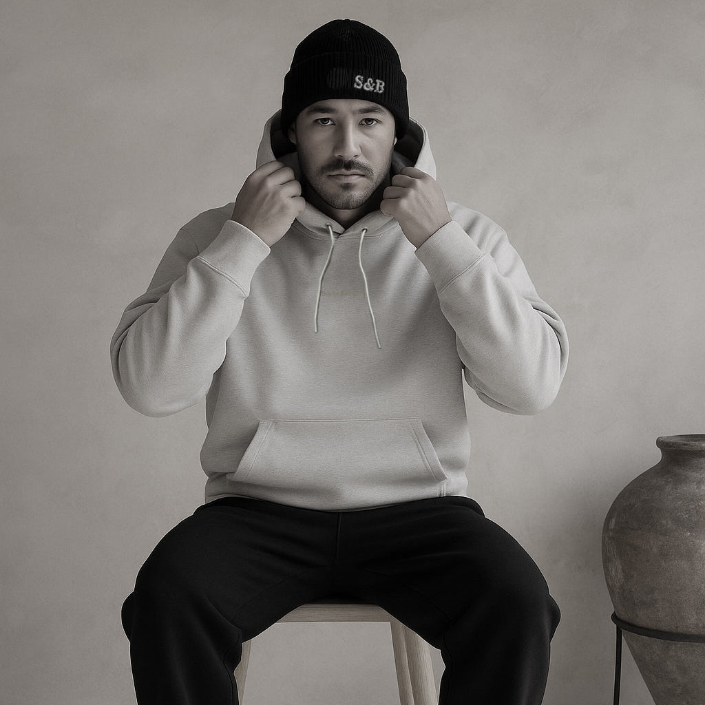 Model wearing Daub Hoody in light grey seated indoors by Sauce & Brown