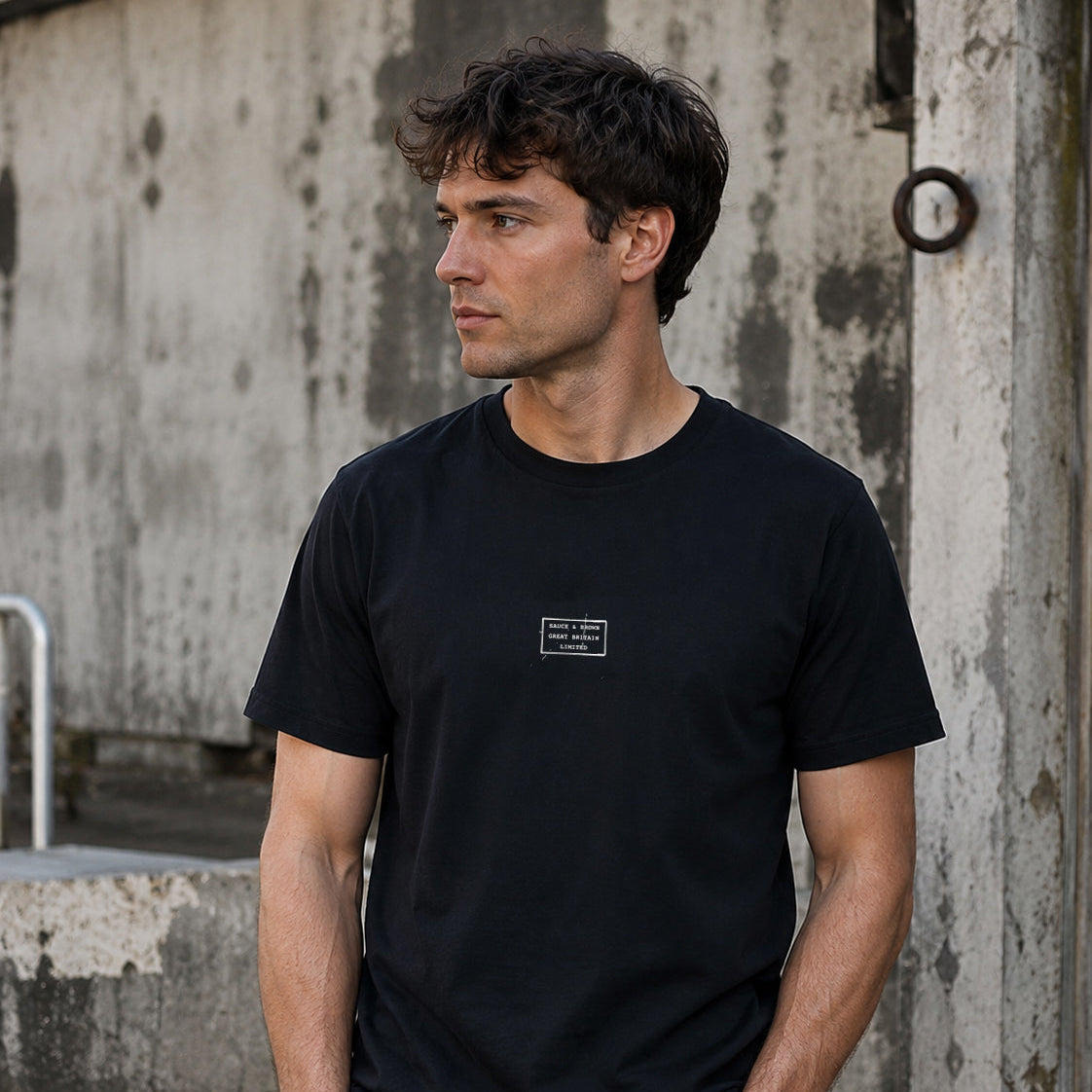 Male model wearing the Sauce & Brown Scratchback black T-Shirt featuring the signature Scratchback chest patch in an urban setting.
