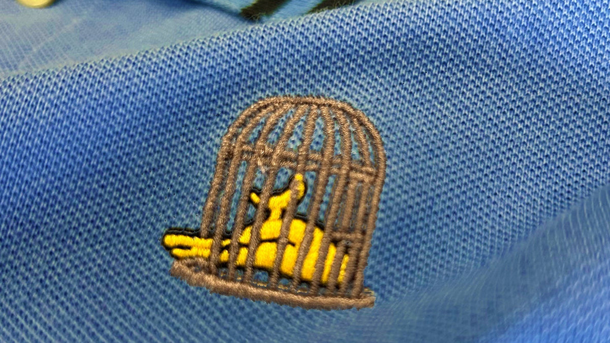 Close-up of blue cotton polo shirt with signature birdcage embroidery detail and textured fabric